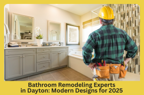 Man in a yellow construction helmet and tool belt standing in a modern bathroom with gray cabinets and a bathtub.