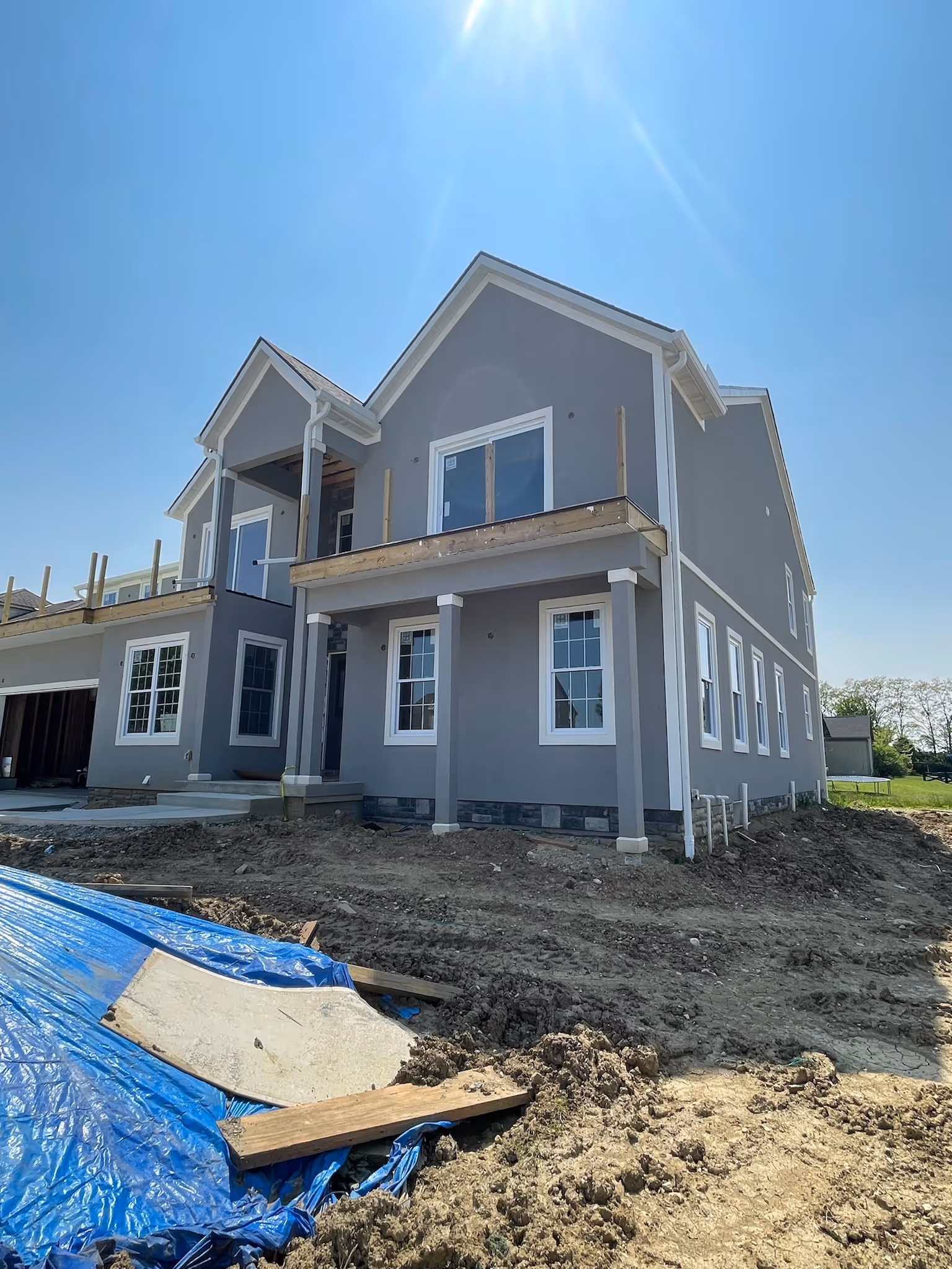Newly constructed two-story gray house with white trim on a sunny day, surrounded by dirt and construction materials.